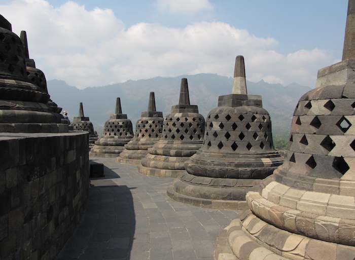 Stupas at Borobudur Buddhist temple in Java, Indonesia. photo of stupas at Borobudur Buddhist temple with mountains in the background