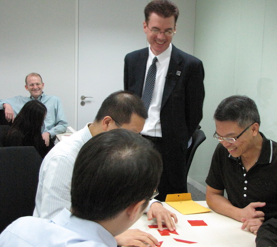 photo of several people around a table smiling with red plastic pieces on the table.