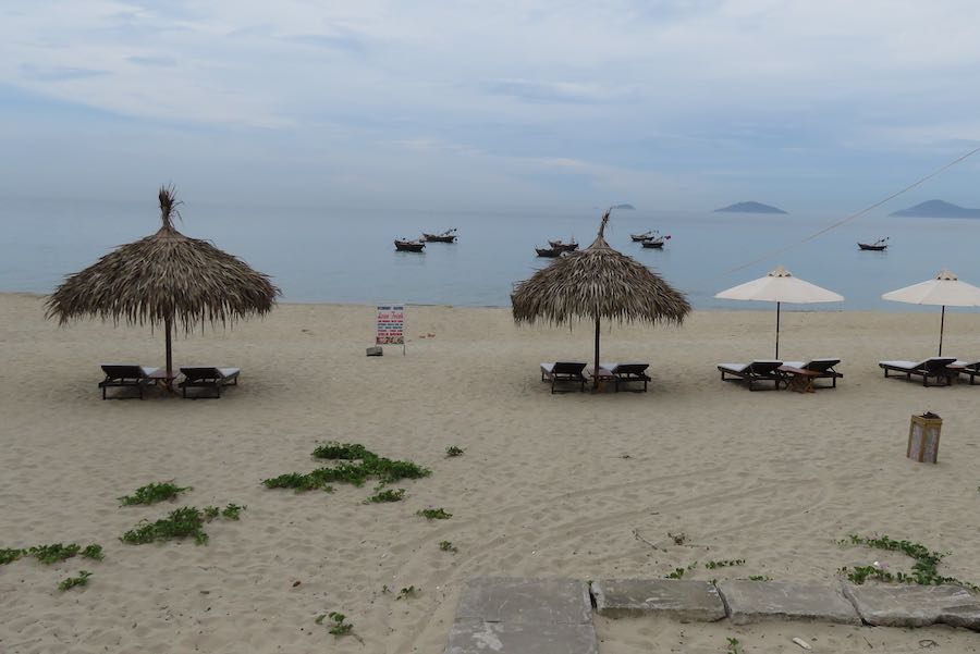Beach with reclining chairs and thatched toped umbrella looking into the ocean with small boats in the view